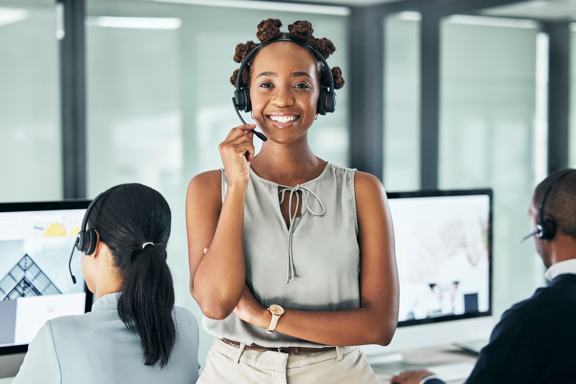 Friendly call center agent standing with arms crossed, looking proud and wearing a headset in an of